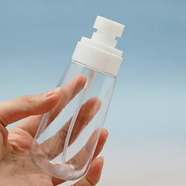 Hand holding a clear plastic fine mist spray bottle with a white pump, showing its sleek, portable design